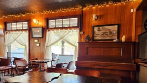 A restaurant interior with wooden walls, framed pictures, and string lights. Tables and chairs are arranged for dining. - Salmo Hotel (Salmo)