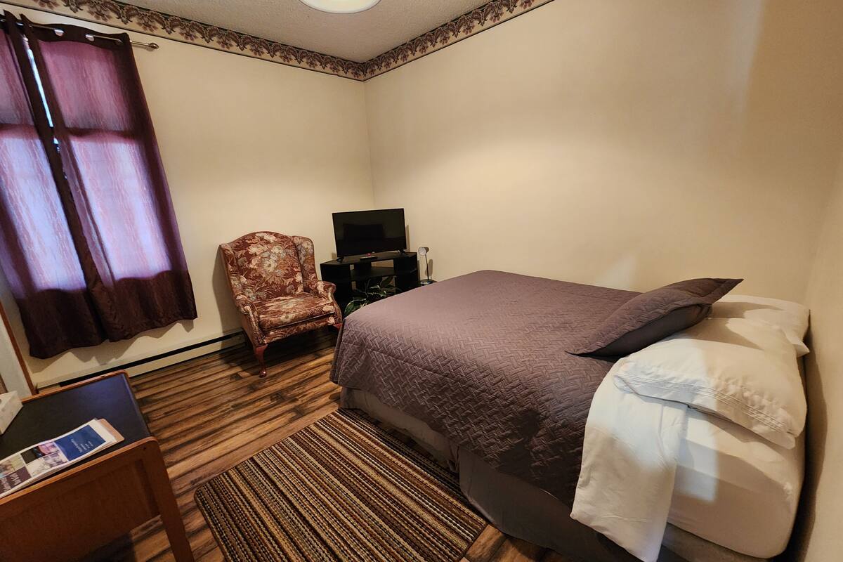 A hotel room with a bed, a chair, a TV, and a small table.