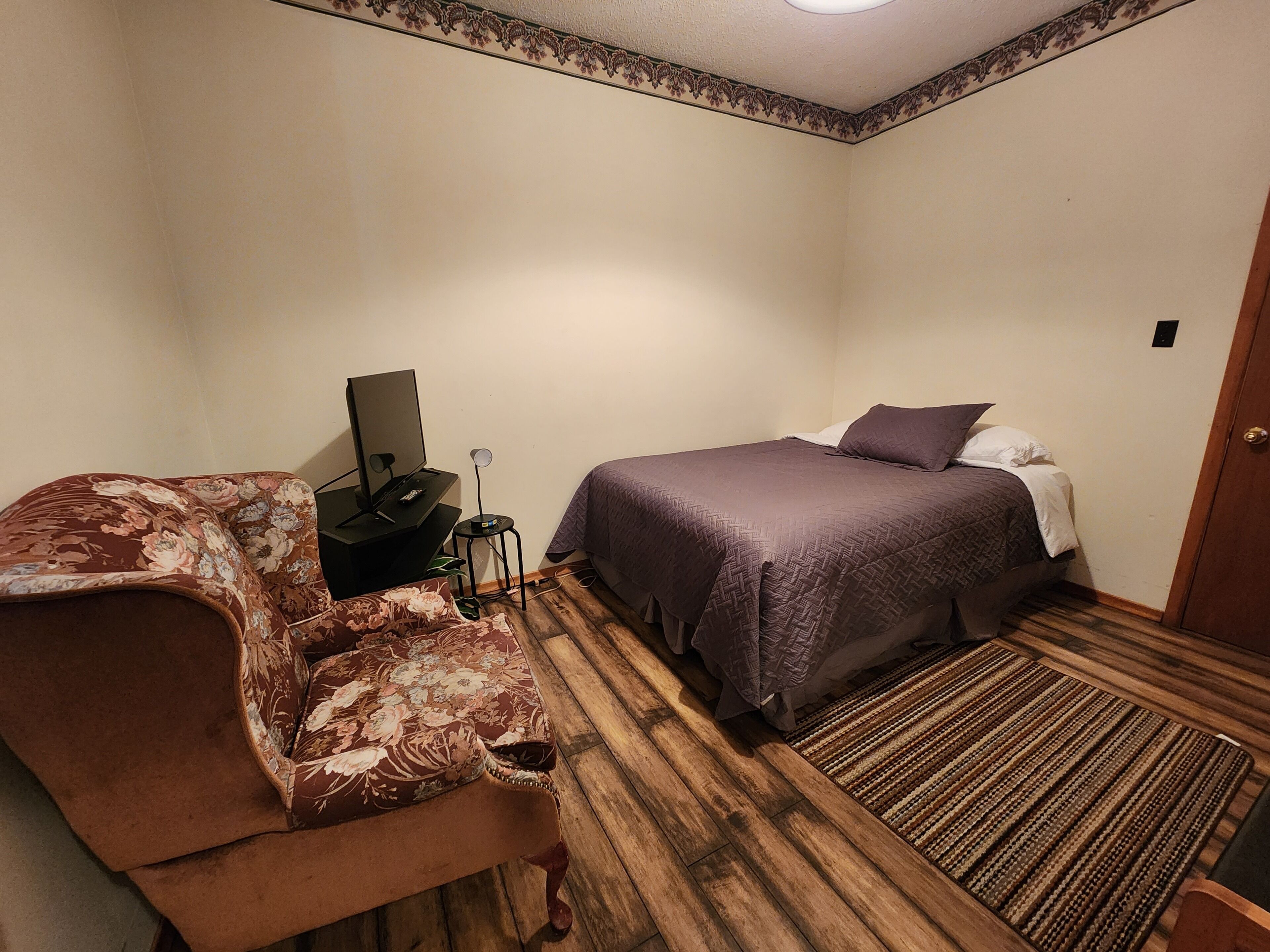 A hotel room with a bed, a sofa, a desk with a computer, and a small table with a lamp.
