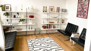 Una sala de estar moderna con una estantería blanca, sillones de cuero negro y una alfombra de lunares.