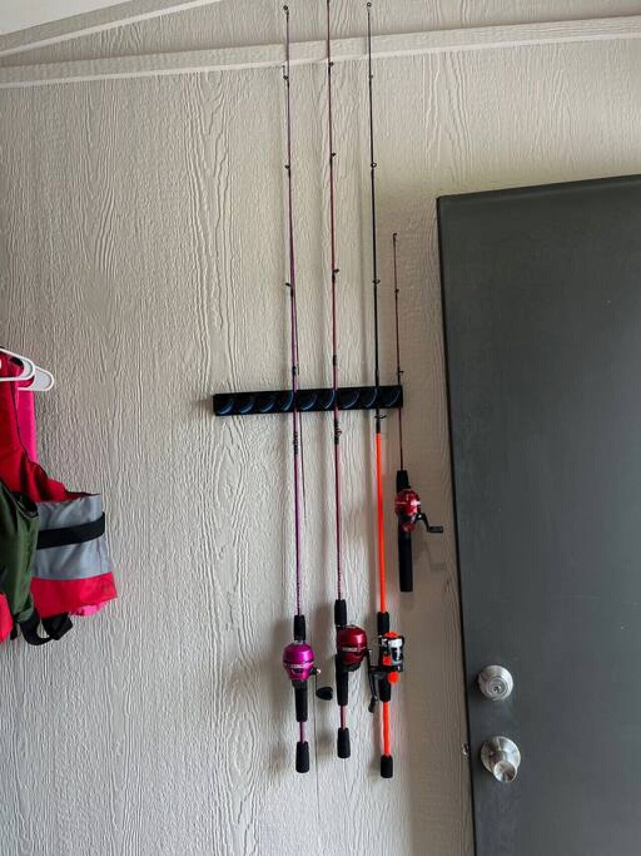 A room with a white textured wall, a black door, and fishing rods hanging on the wall.