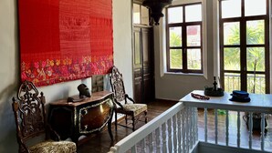 A room with a large red tapestry, a wooden cabinet, a chandelier, and a view of greenery through large windows. - The Thirty8 Heritage House (Chania)