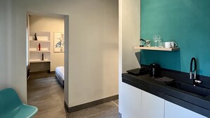 A modern kitchen with a teal accent wall, a black countertop, and a sink. There is a chair and a table in the foreground, and a bed in the background. - The Thirty8 Heritage House (Chania)