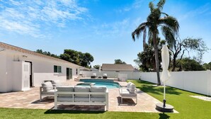 A modern outdoor patio with a pool, white furniture, and a palm tree. - South Tampa Pool Home! (Tampa)