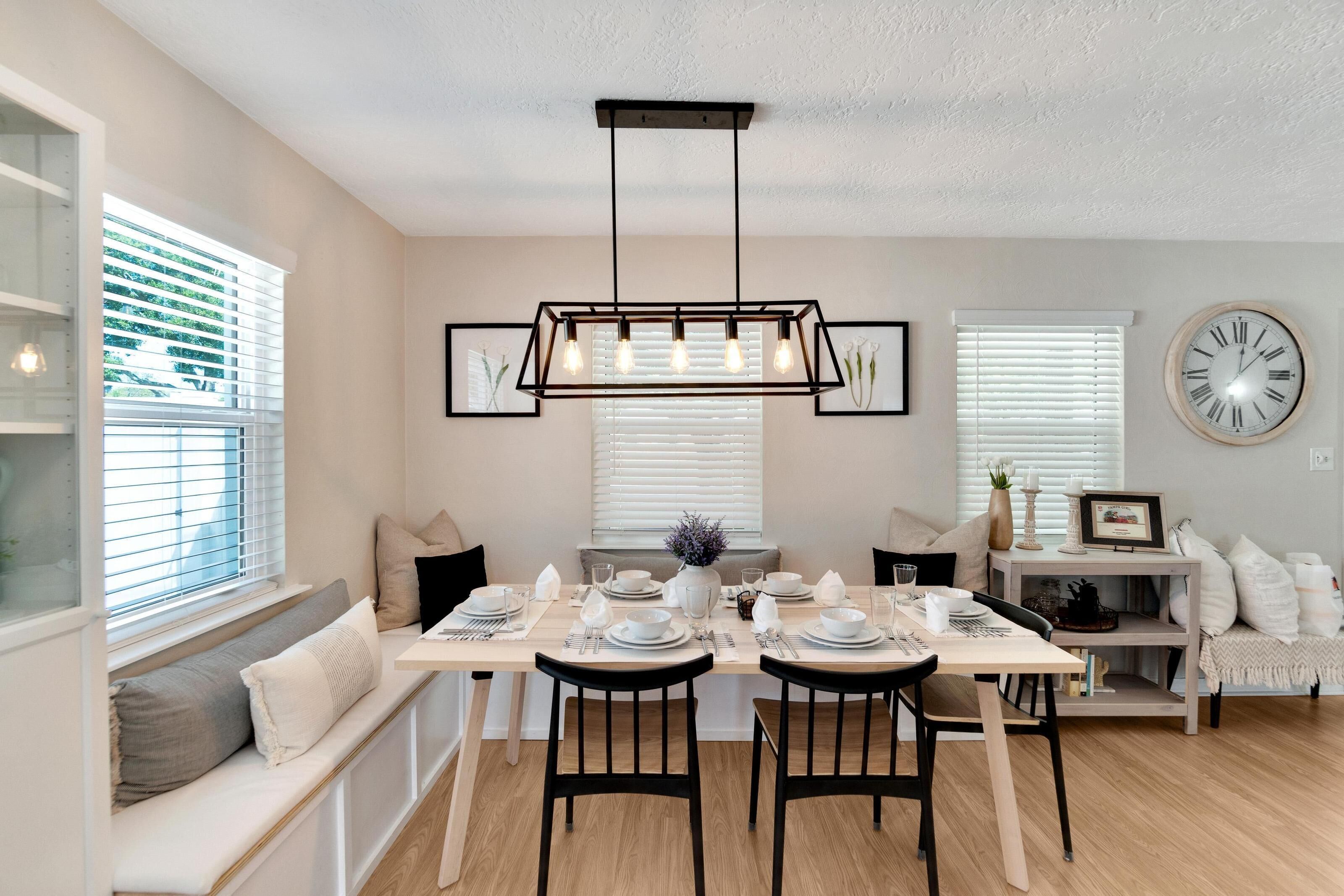 A dining area with a rectangular chandelier, white walls, and a clock on the wall.