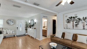 A spacious living room with a wooden floor, a brown leather sofa, a coffee table, and a painting of palm trees. - South Tampa Pool Home! (Tampa)