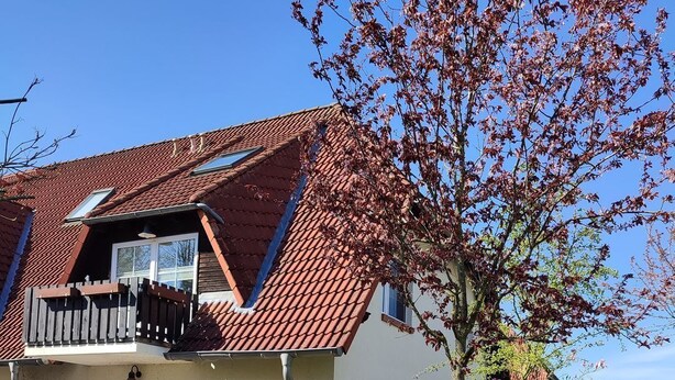 Een huis met twee verdiepingen, een rode pannendak, een balkon en een verzorgd gazon.