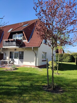 A two-story house with a red-tiled roof, a balcony, and a well-maintained lawn.