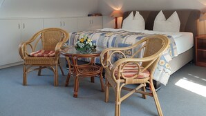 Een slaapkamer met een bed, twee rieten stoelen, een tafeltje met een vaas en een nachtkastje.