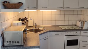 Een moderne keuken met witte kastjes, een granieten aanrechtblad, een inbouwoven en een vaatwasser.