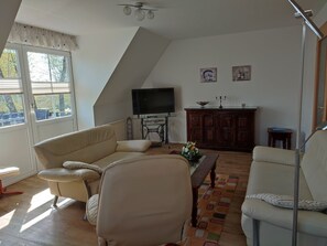 Sala de estar con sofá, sillón, televisor, mueble bajo y una ventana con persianas.