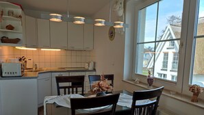 Een compacte keuken met witte kastjes, een eettafel met stoelen en een raam met uitzicht op gebouwen.