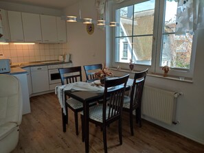 Una cocina moderna con armarios blancos, una mesa de comedor con cuatro sillas y una ventana con vistas al exterior.