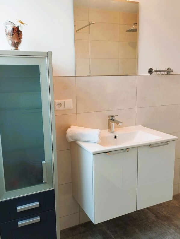 A modern bathroom with a glass-enclosed cabinet, a white sink with a towel, and a shower area.