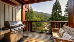 A wooden deck with a grill, a cushioned bench, and a view of a forested mountain. - Ski-In/Ski-Out | Spacious 4BR | Hot Tub | Gear Storage Garage | Managed by Aloha Whistler (Whistler)
