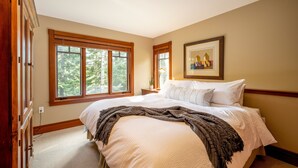 A bedroom with a large bed, wooden window frames, a framed picture on the wall, and a view of trees outside. - Ski-In/Ski-Out | Spacious 4BR | Hot Tub | Gear Storage Garage | Managed by Aloha Whistler (Whistler)