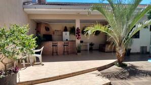 A covered patio area with a brick floor, two bar stools, a white table, and a potted plant. - Edicula Foz (Foz do Iguaçu)