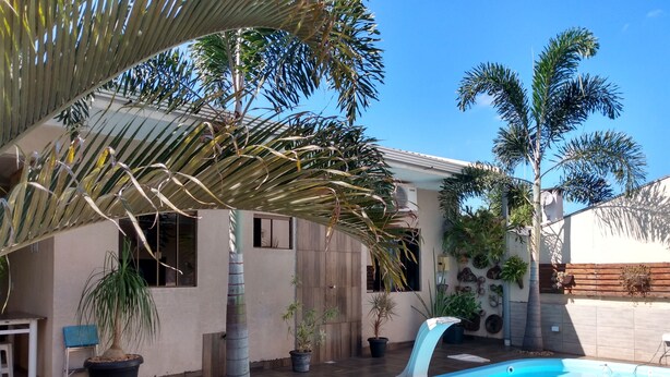 A backyard with a swimming pool, palm trees, and a house with a tiled patio. - Edicula Foz (Foz do Iguaçu)