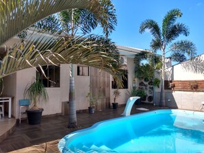 Un jardin avec une piscine, des palmiers et une maison dotée d’une terrasse carrelée.