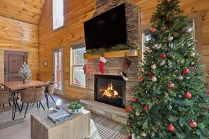 A cozy log cabin interior with a fireplace, a Christmas tree, and a television mounted on the wall.