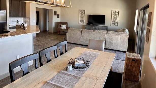 Une cuisine moderne avec des meubles de couleur sombre, un îlot central intégré et un coin repas comprenant une table et des chaises en bois.