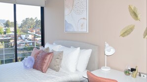Habitación de hotel moderna con una cama grande, un escritorio, una lámpara de escritorio y vistas de la ciudad a través de amplios ventanales.
