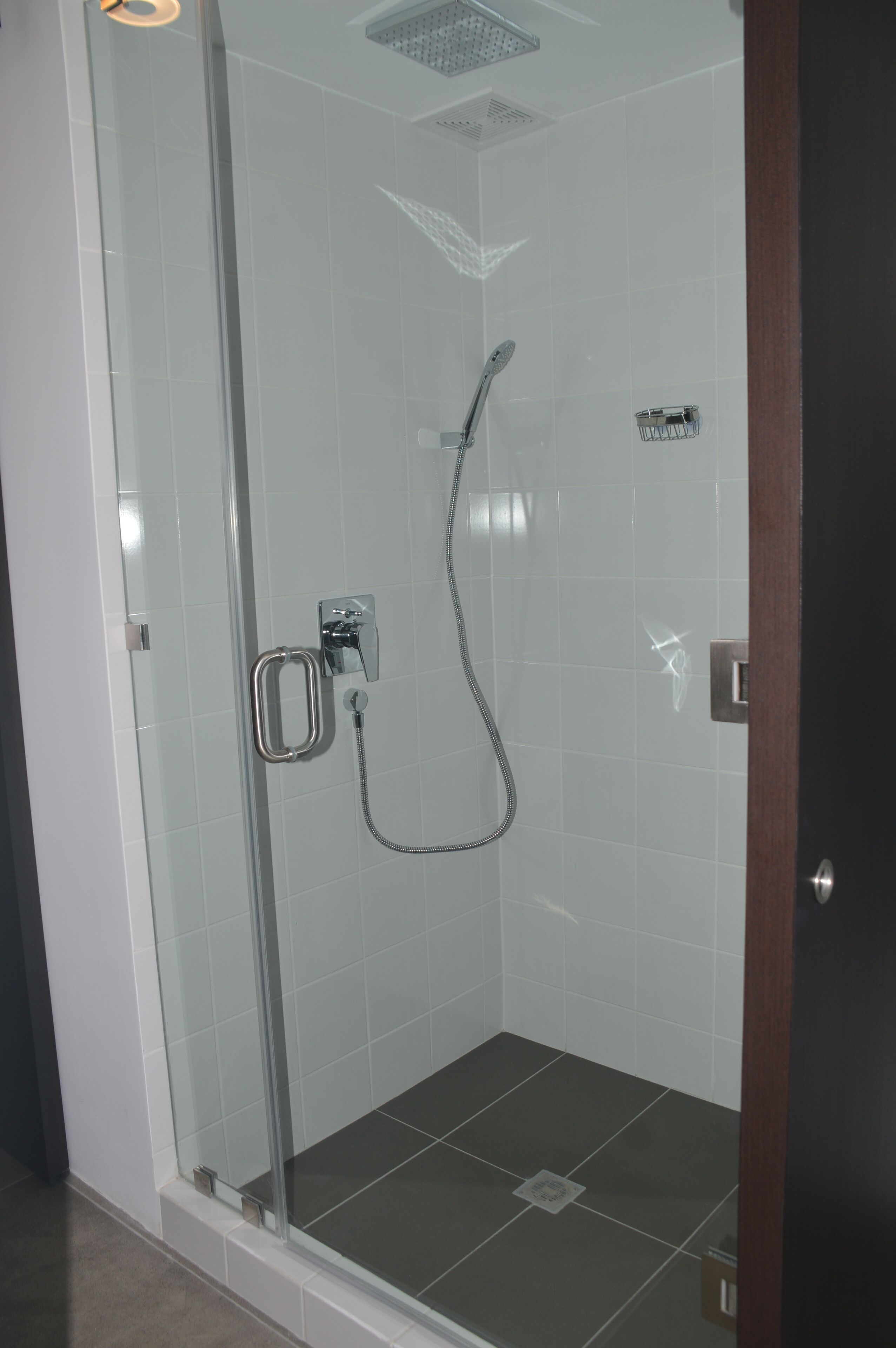 Ducha con cerramiento de vidrio, cabezal de ducha de mano y llave instalada en la pared.
