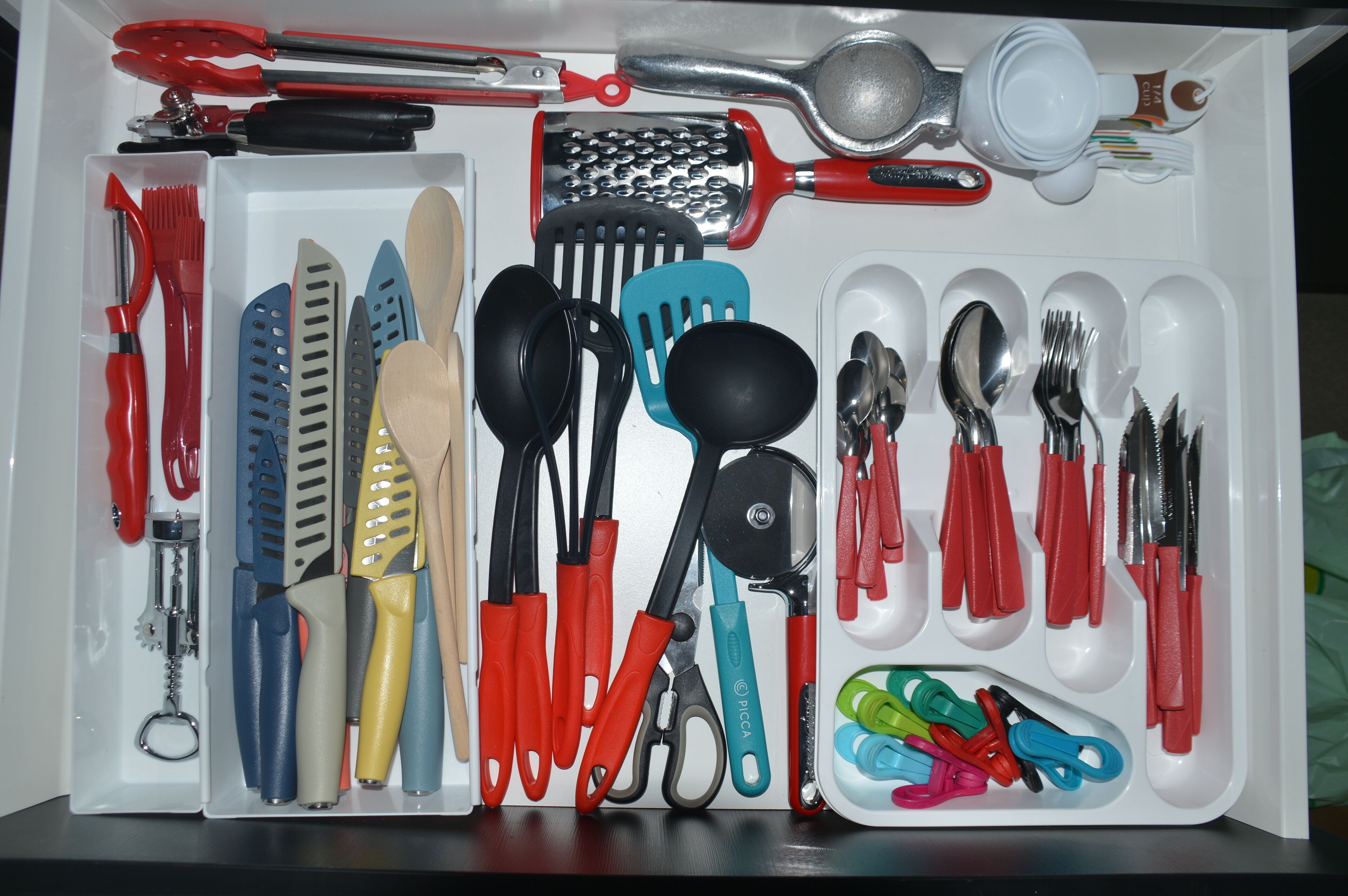 Un tiroir contenant divers ustensiles et outils de cuisine, notamment des ciseaux, des spatules et une râpe.