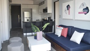 Una sala de estar moderna con un sofá azul oscuro, una mesa de centro blanca y una cocina al fondo.