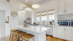 Una cocina moderna con una isla grande, taburetes de bar, armarios blancos y un microondas.