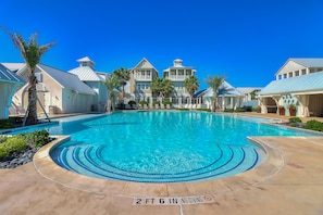 A swimming pool with a 2 ft 6 in no diving sign, surrounded by palm trees and a large building with multiple balconies. - Dazzling home with a balcony and updated appliances - pool, gym, & on-site golf (Port Aransas)