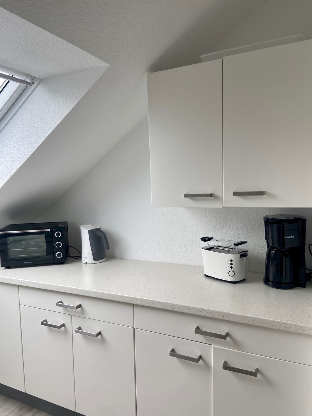 A modern kitchen with white cabinets, a built-in toaster, a coffee maker, and a microwave.