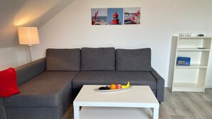 Een moderne woonkamer met een grijze modulaire bank, een witte salontafel met fruit, een lamp en een witte boekenkast.