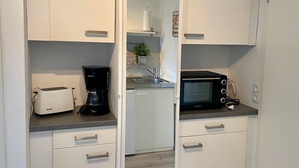 Een kleine keuken met witte kastjes, een broodrooster, een koffiezetapparaat, een magnetron en een klein spoelbakje.