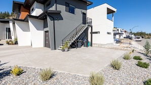 Ein modernes, zweistöckiges Haus mit Betonauffahrt, einer Treppe, die zum oberen Stockwerk führt, und einem kleinen Garten mit Pflanzen und Steinen.
