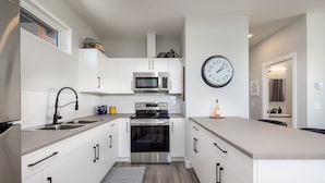 Eine moderne Küche mit weißen Schränken, Edelstahlgeräten und einer Uhr an der Wand.