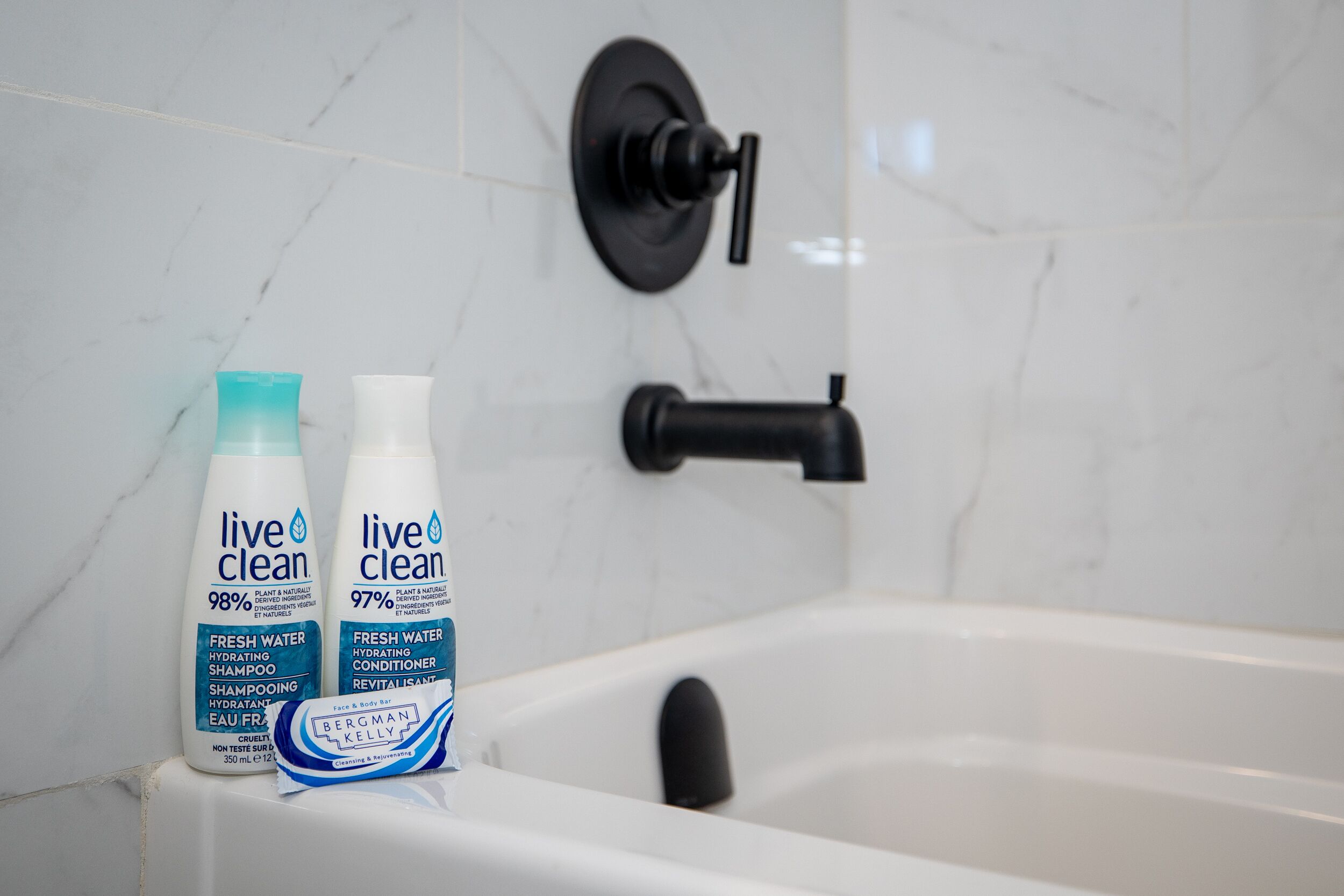 A bathroom with a white bathtub, two bottles of 'live clean' shampoo, and a black faucet.