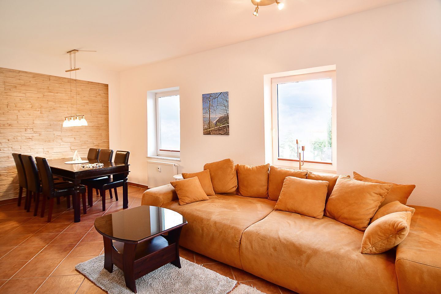 A living room with a sofa, a dining table with chairs, a piano, and a window with a view.