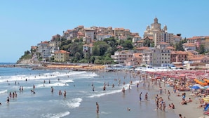 A crowded beach with people swimming and sunbathing, and a large building complex in the background. - Lovely apartment in villa for 4 guests with WIFI, A/C, patio and pets allowed (Imperia)