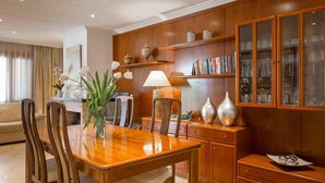 Un coin repas avec une table en bois, des chaises, un vase de fleurs, une lampe et un meuble avec des portes en verre contenant des livres et de la verrerie.