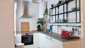 Une cuisine moderne avec des armoires blanches, une hotte de cuisinière en acier inoxydable, un four encastré, un lave-vaisselle et un plan de travail sur lequel se trouve un grille-pain rouge.
