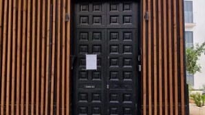 Une porte noire ornée d’un motif quadrillé, flanquée de lattes de bois verticales.