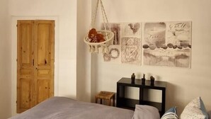 Une chambre à coucher avec un lit, une porte en bois, un panier suspendu contenant divers objets et des œuvres d’art mural.