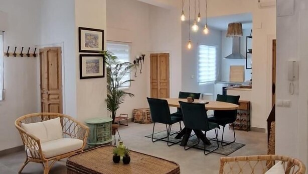 Un vaste espace de vie comprenant une table et des chaises, un canapé en osier et un luminaire suspendu.