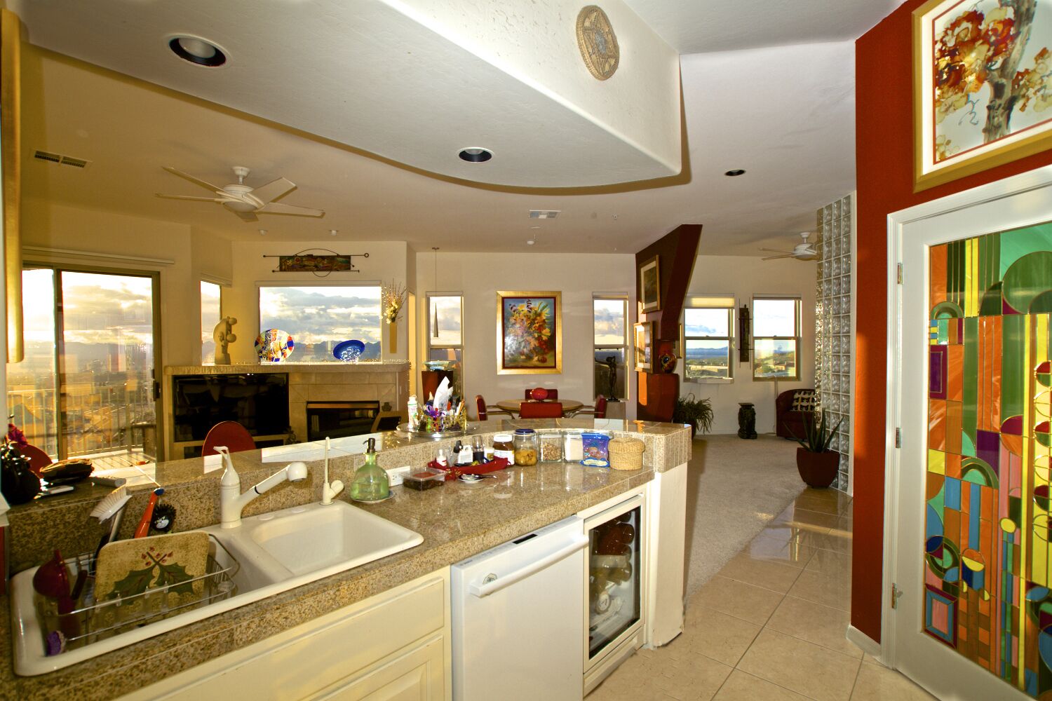 A spacious kitchen with granite countertops, a dishwasher, and a large island with a sink. There are multiple windows providing natural light and a view of the outdoors.