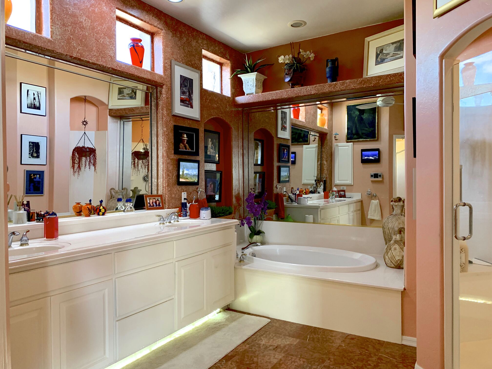 A spacious bathroom with a large bathtub, double sinks, and multiple framed pictures on the walls.