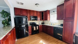 Une cuisine avec des meubles de rangement en bois, un réfrigérateur noir, un four à micro-ondes, une cuisinière et un lave-vaisselle.