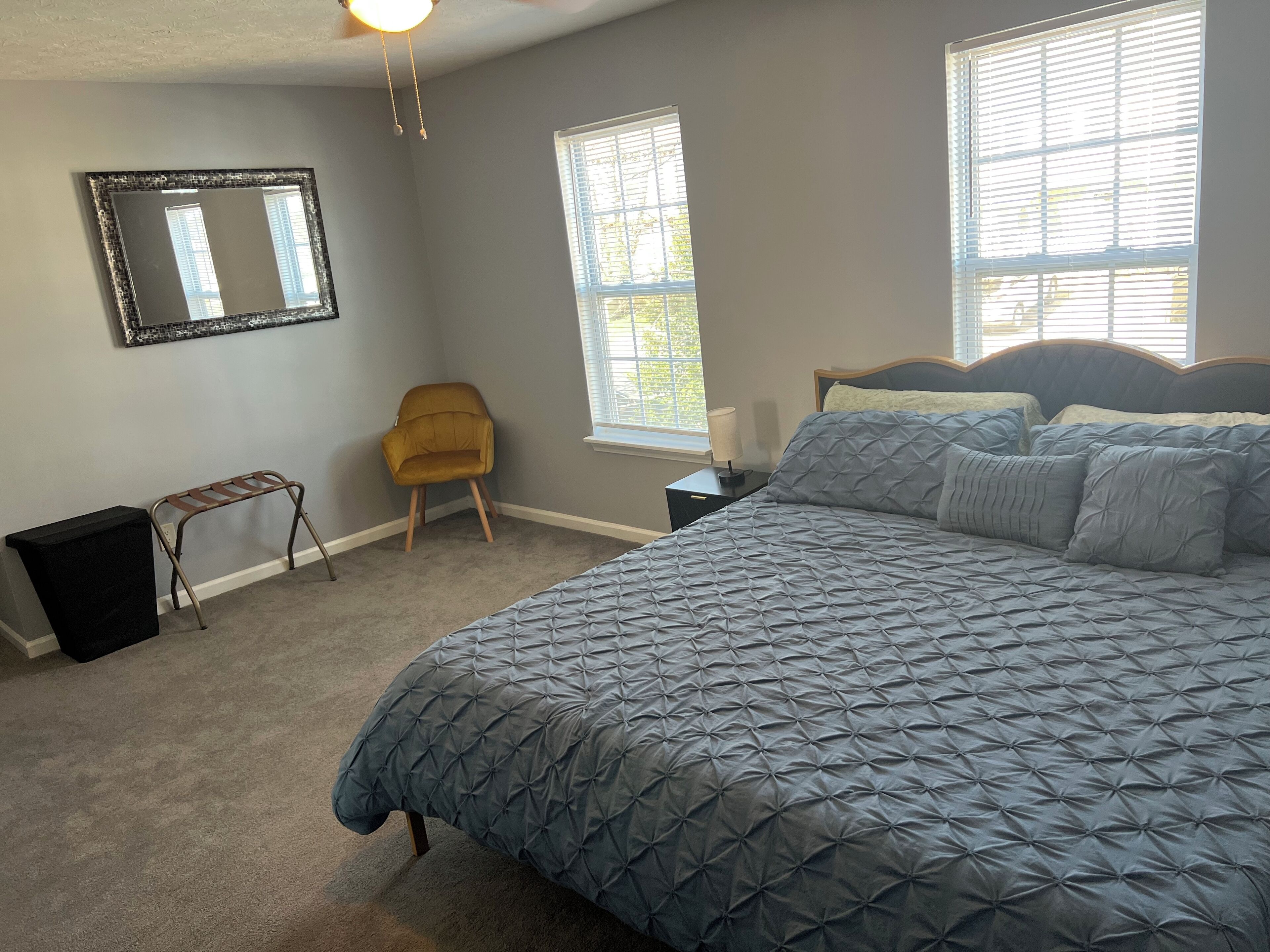 Een slaapkamer met een groot bed, een stoel, een klein tafeltje en een spiegel aan de muur.