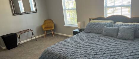 Een slaapkamer met een groot bed, een stoel, een klein tafeltje en een spiegel aan de muur.