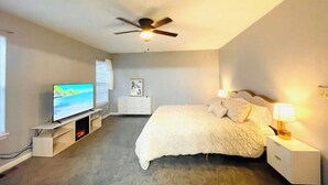 Une chambre à coucher avec un lit, un téléviseur posé sur un meuble, un ventilateur de plafond et des lampes de chevet.